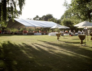 A photo of a large dinner reception under a large white Made in the Shade tent with a large grassy field in the foreground